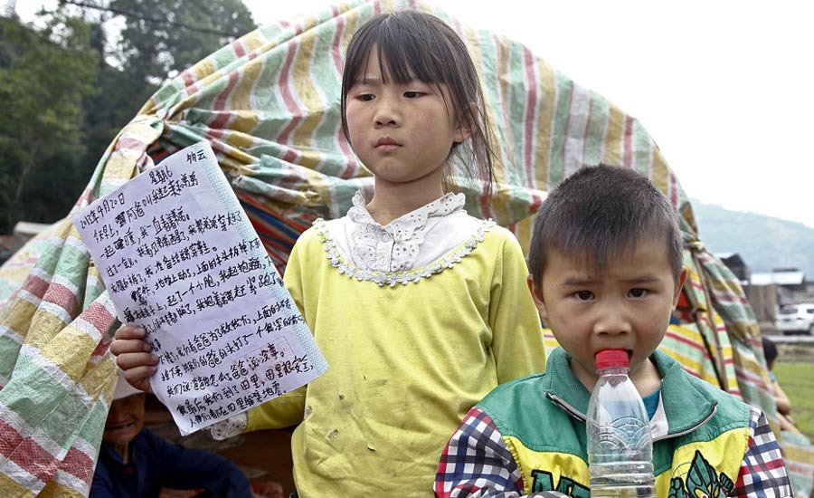 雅安“小英雄”的地震日记  4月21日，四川雅安地震重灾区芦山龙门乡，在一个农田里的自制简易“抗震棚”外，9岁的姐姐高梦思正在展示她在20日地震时救出身旁弟弟后写的日记。中新社发 张浩 摄